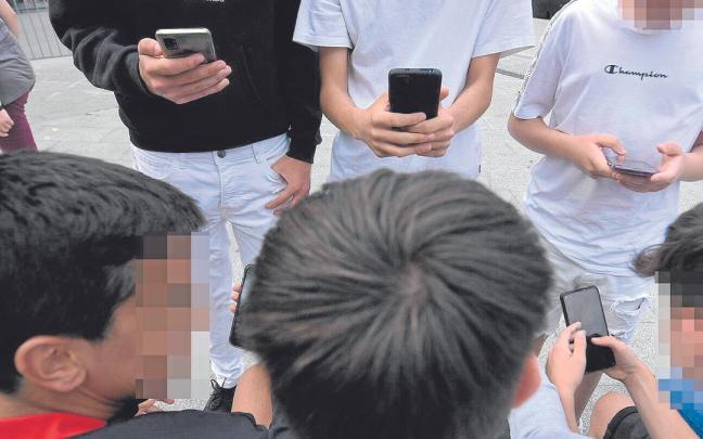 Un grupo de menores, ajenos a esta información, consultan sus teléfonos móviles reunidos en una calle de Bilbao.