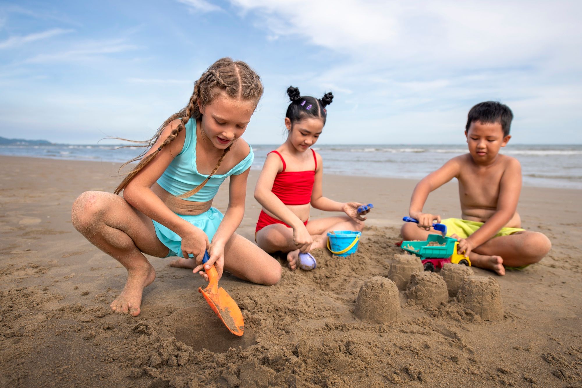 Dos niñas y un niño juegan con la arena en la playa.