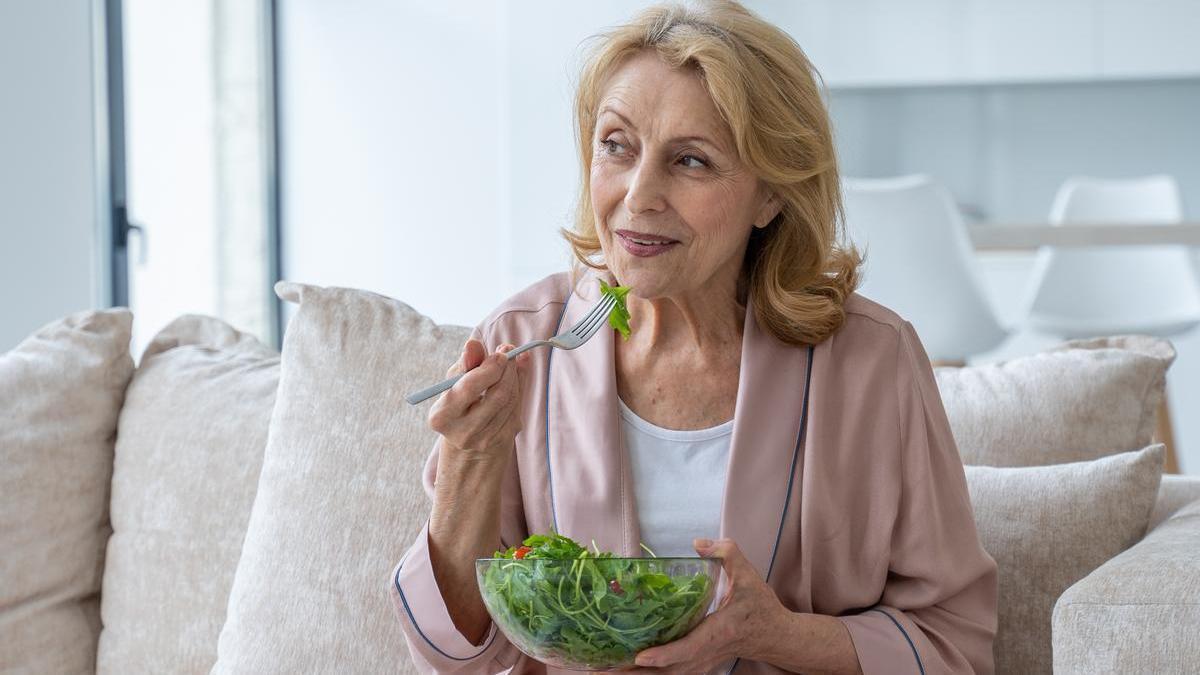 Mujer come una ensalada sentada en el sofá.