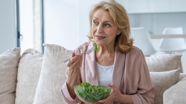 Mujer come una ensalada sentada en el sofá.
