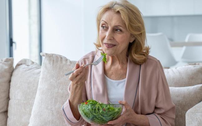 Mujer come una ensalada sentada en el sofá.