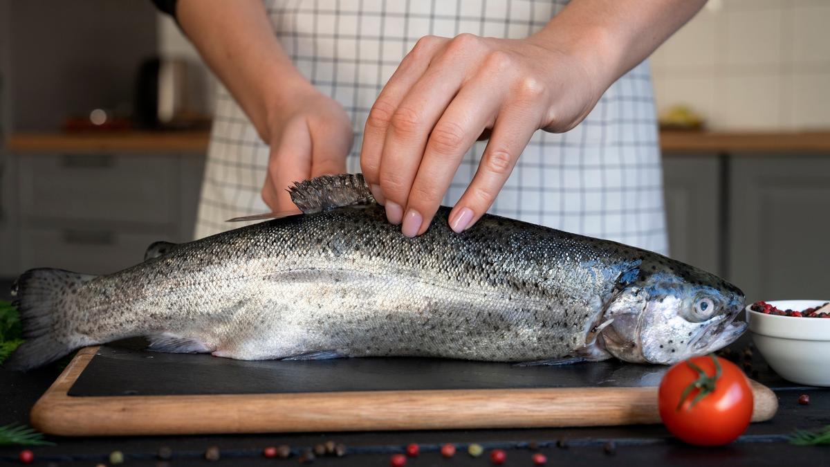 Una mujer prepara un pescado para meterlo al horno.