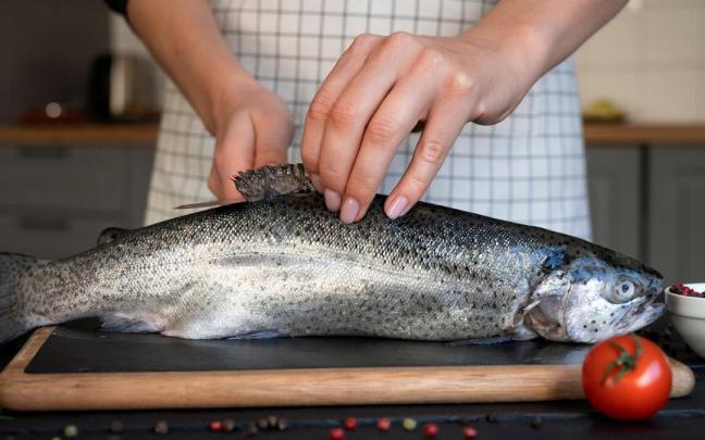 Una mujer prepara un pescado para meterlo al horno.