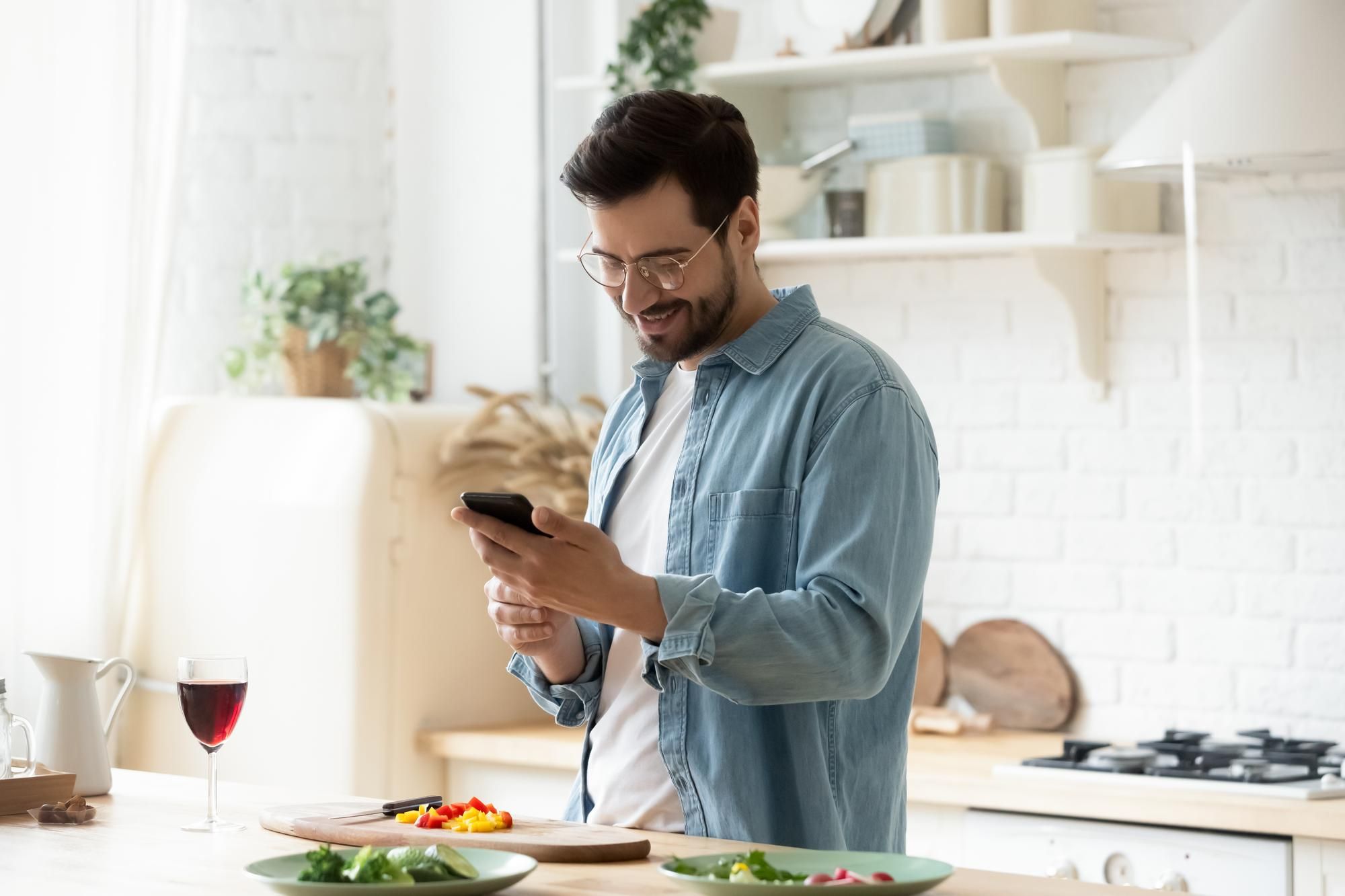 Un hombre chatea con el móvil mientras prepara la comida.
