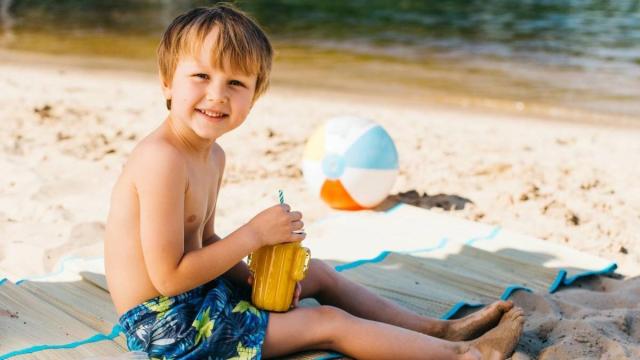 Niño sentado en su toalla en la playa.