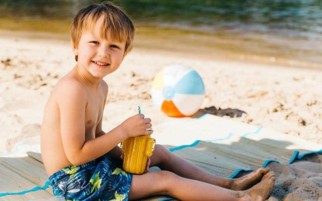 Niño sentado en su toalla en la playa.