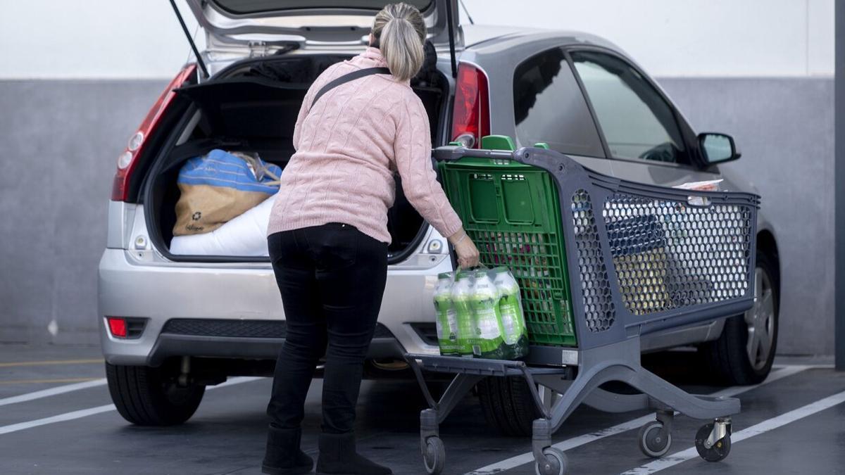 Una mujer carga la compra en el maletero del coche.