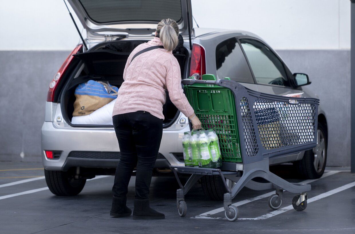 Una mujer carga la compra en el maletero del coche.