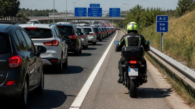 Una moto adelanta por el arcén derecho a los coches retenidos por un atasco en una autovía.