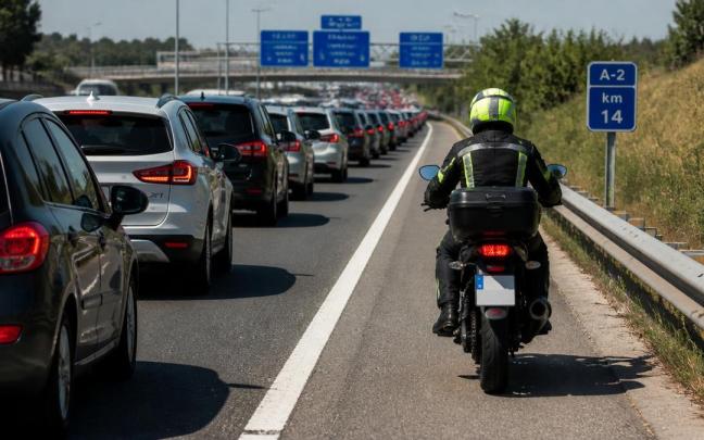 Una moto adelanta por el arcén derecho a los coches retenidos por un atasco en una autovía.