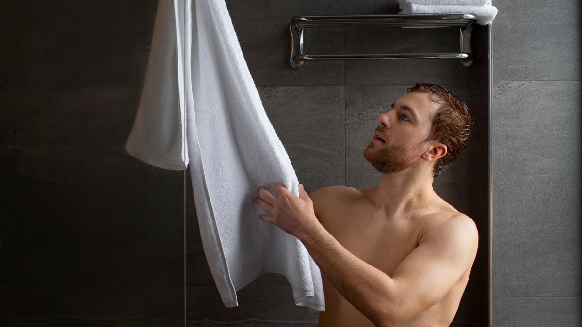 Un hombre coge una toalla para secarse al salir de la ducha.