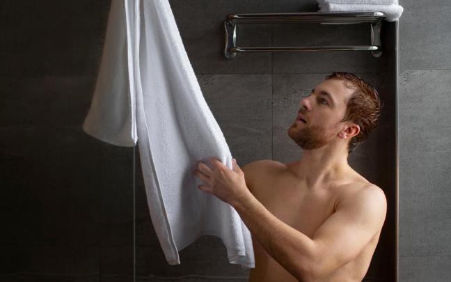 Un hombre coge una toalla para secarse al salir de la ducha.