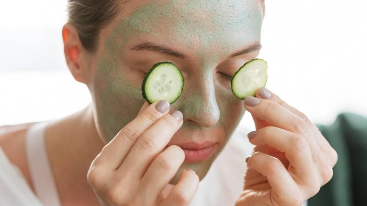 Chica con una mascarilla de arcilla en la cara y dos rodajas de pepino para reducir las bolsas y ojeras en los ojos