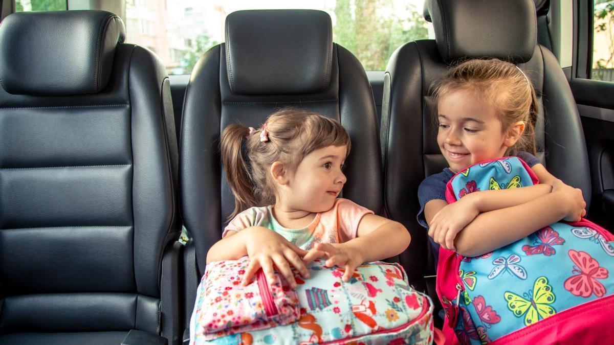 Niñas sentadas en el coche junto a sus mochilas.
