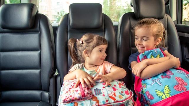 Niñas sentadas en el coche junto a sus mochilas.