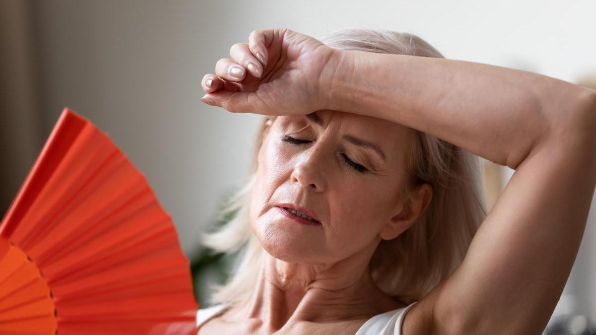 Mujer se abanica con un abanico rojo para sobrellevar mejor las altas temperaturas.