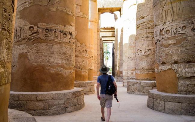 Un turista camina entre las columnas de un templo egipcio.