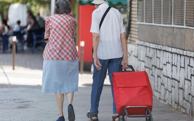 Una pareja mayor camina con un carro de la compra.