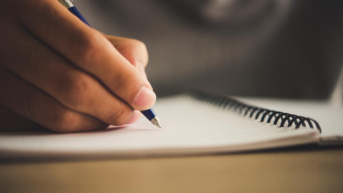 Una persona escribiendo en un cuaderno con un boligrafo. FREEPIK