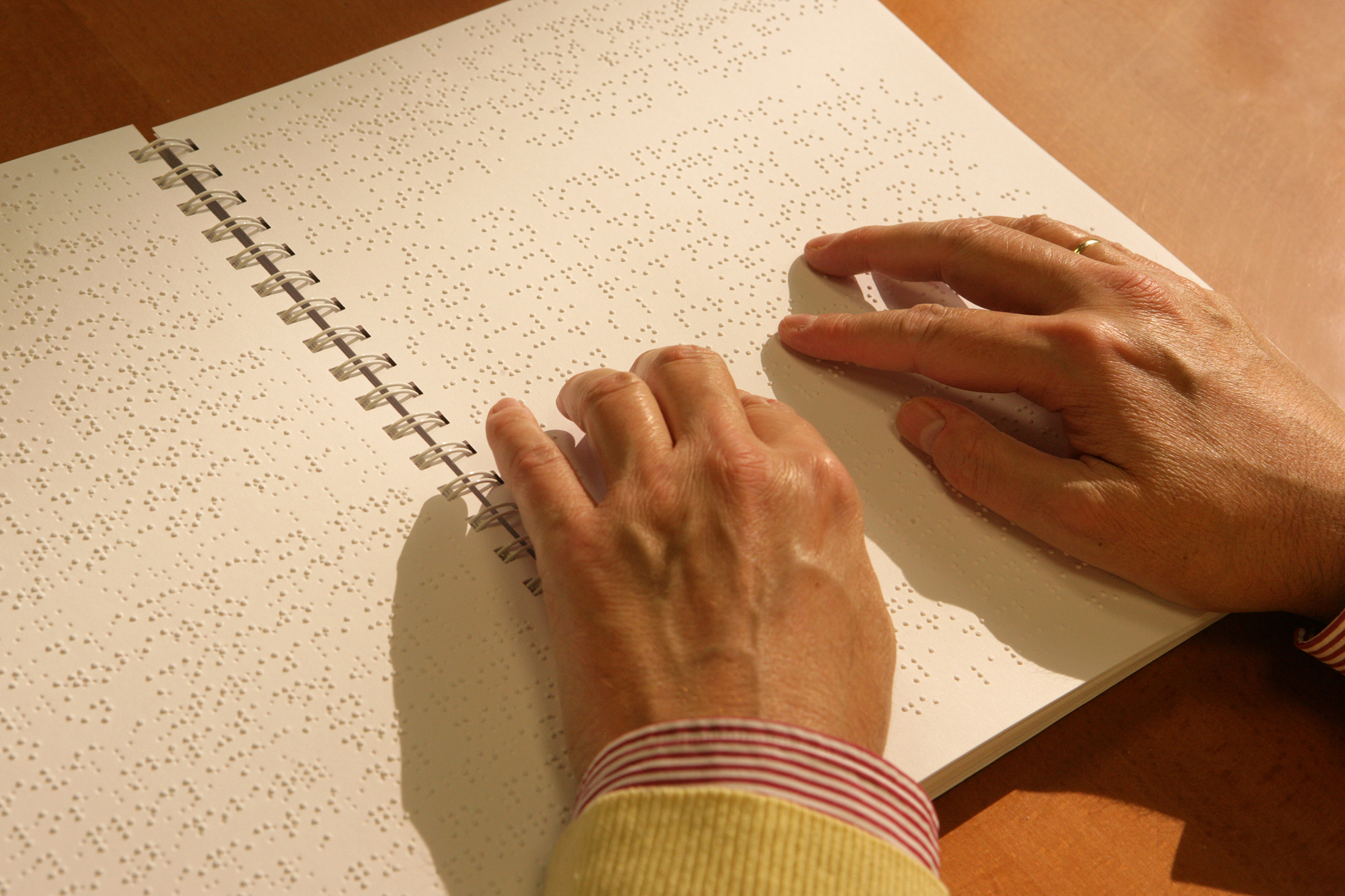 Las manos de una persona ciega leen un libro en Braille. ONCE