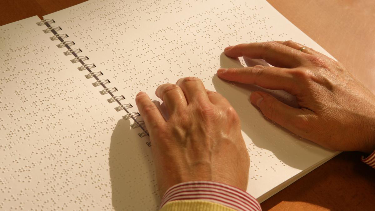 Las manos de una persona ciega leen un libro en Braille. ONCE