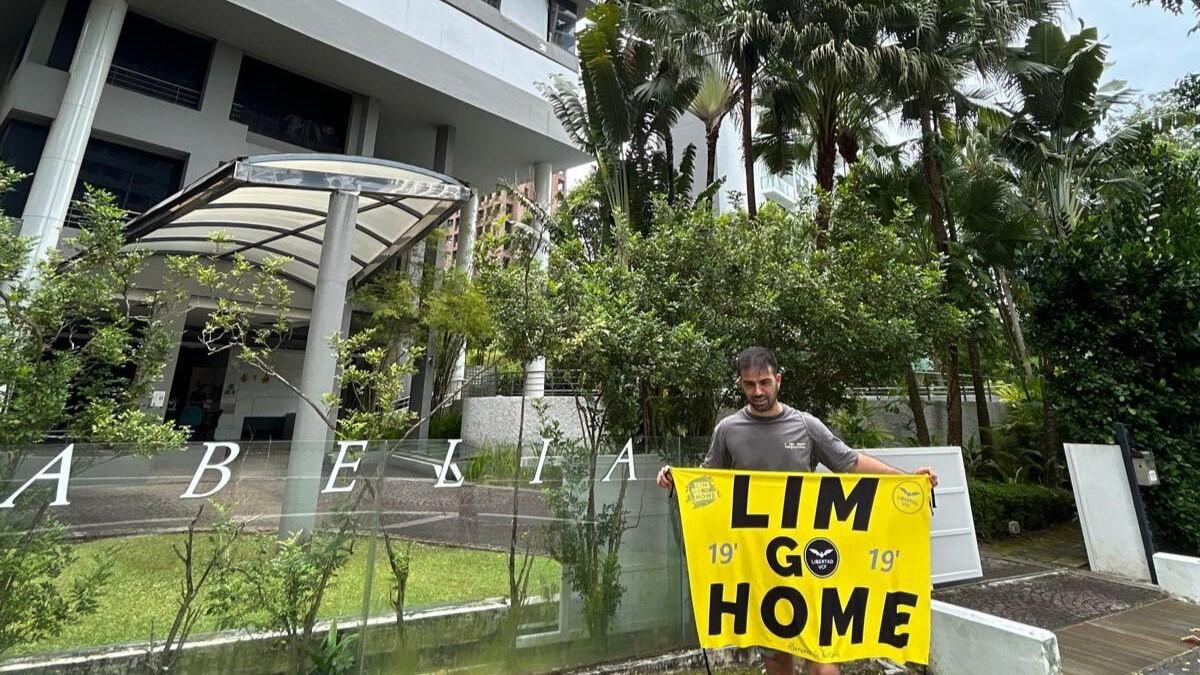 Imagen del detenido junto al cartel reivindicativo ante uno de los edificios de Peter Lim | Foto: X