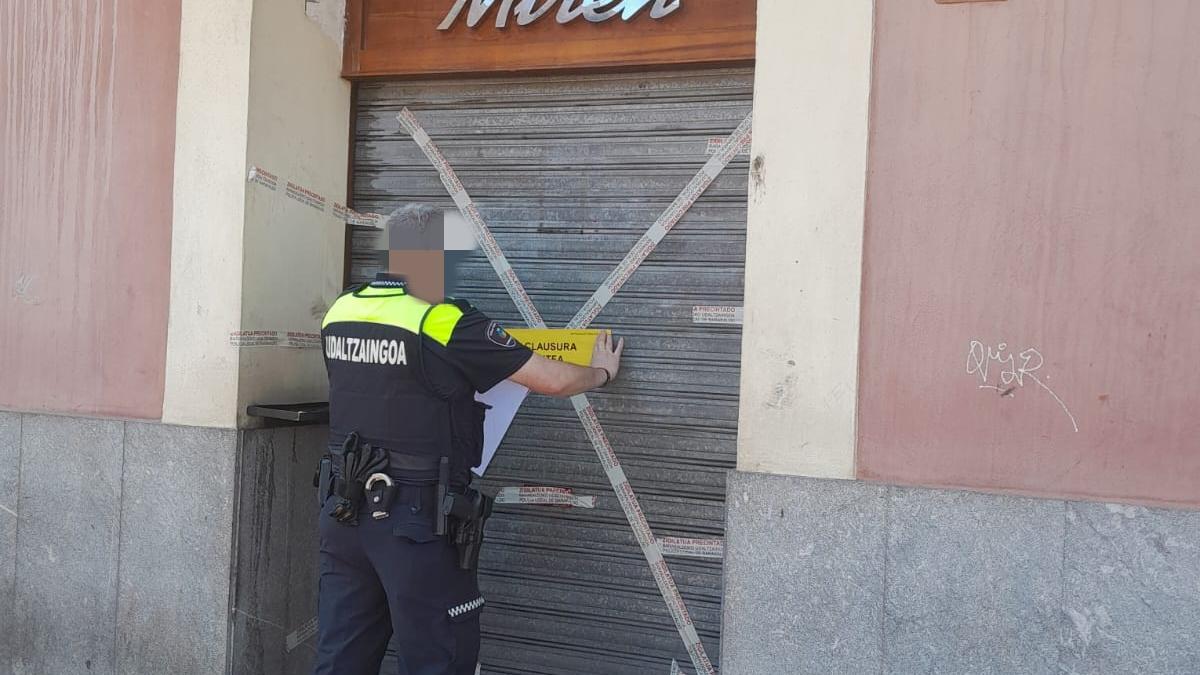 Un agente de la Policía Local colocando el precinto en la puerta de entrada al bar Miren | AYTO BARAKALDO