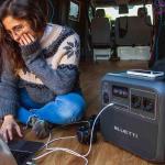 Una joven teletrabaja en su furgoneta utilizando una estación de energía portátil para cargar sus dispositivos