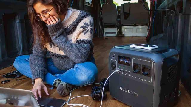 Una joven teletrabaja en su furgoneta utilizando una estación de energía portátil para cargar sus dispositivos